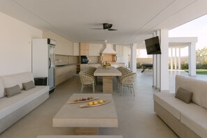 A modern kitchen with a dining area, a flat-screen TV mounted on a column, and a pool table in the background. - Anassa Villa, with 110m² Pool & Emerald Gardens (Rethymno)