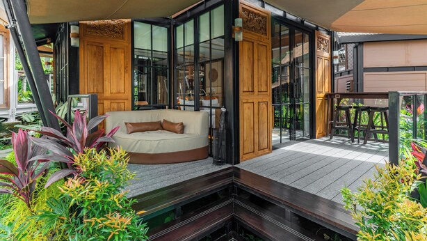 A modern outdoor living area with a wooden deck, a sofa, and a dining table. - Desa La Casa Modular (Ubud)