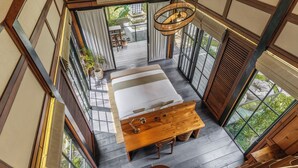 A high-ceilinged room with a large bed, wooden furniture, and a view of an outdoor garden. - Desa La Casa Modular (Ubud)