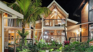 A two-story wooden house with a balcony, surrounded by tropical plants. - Desa La Casa Modular (Ubud)