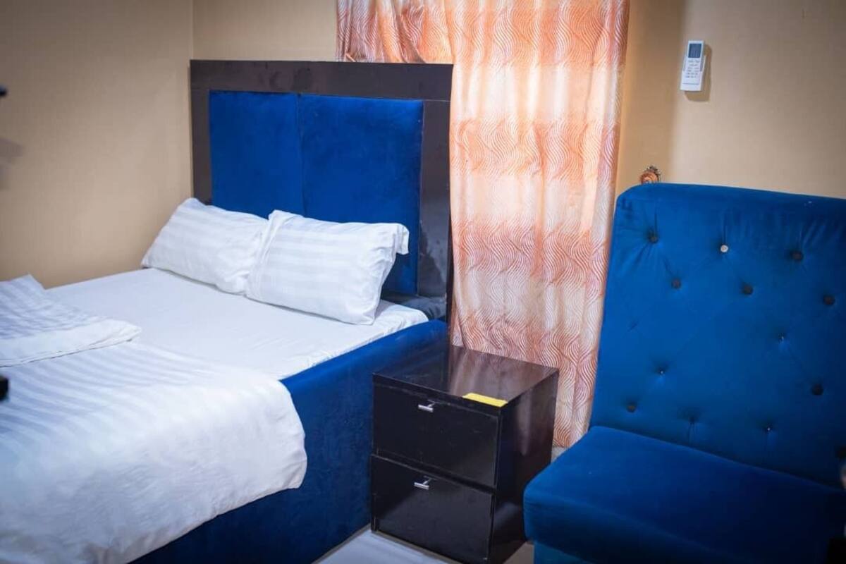 A hotel room with a bed, a bedside table, and a blue armchair.