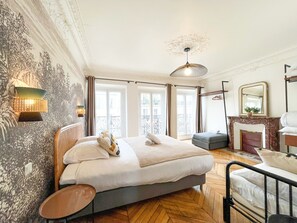 A bedroom with a large bed, a small table, a mirror, and a fireplace.