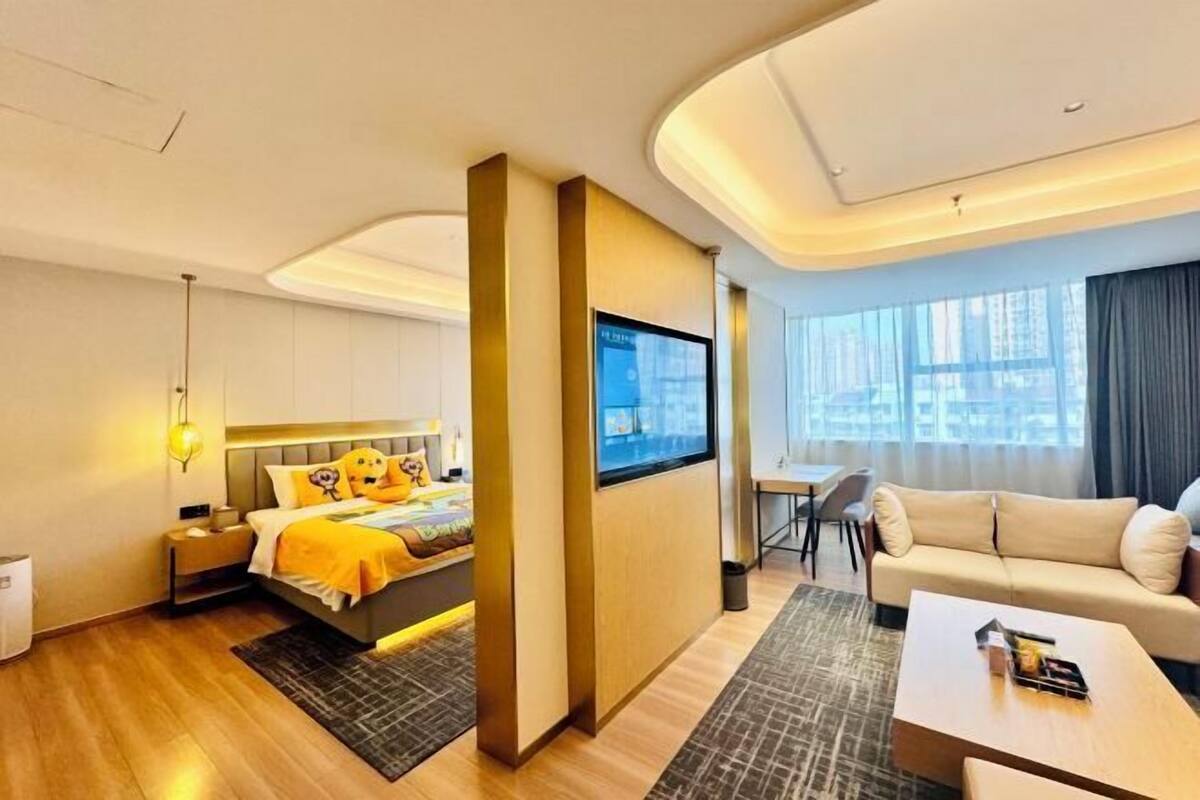 A modern hotel room with a bed, a TV, a sofa, and a desk.