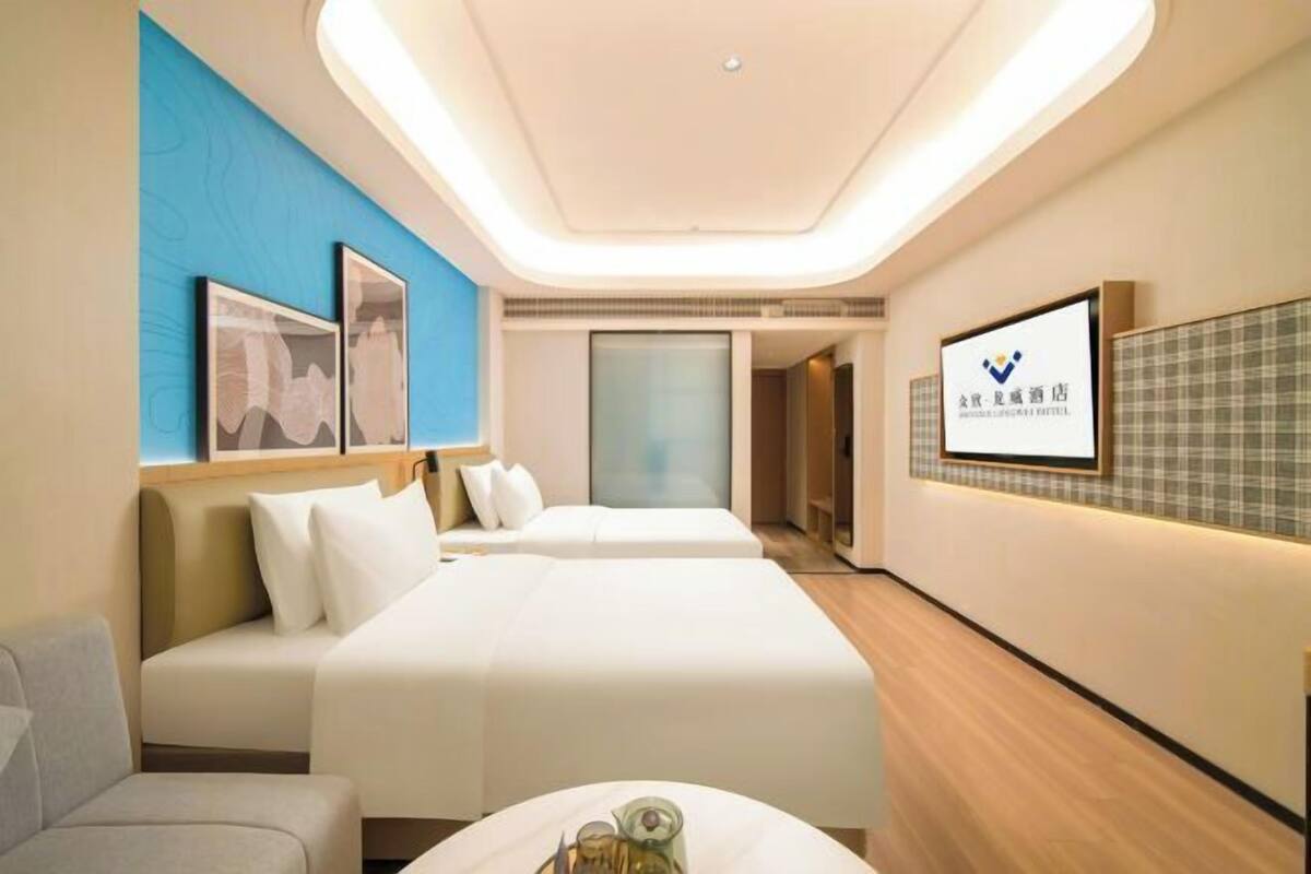A modern hotel room with a bed, a sofa, and a small table with a glass. There are framed pictures on the wall and a sign with Chinese characters.