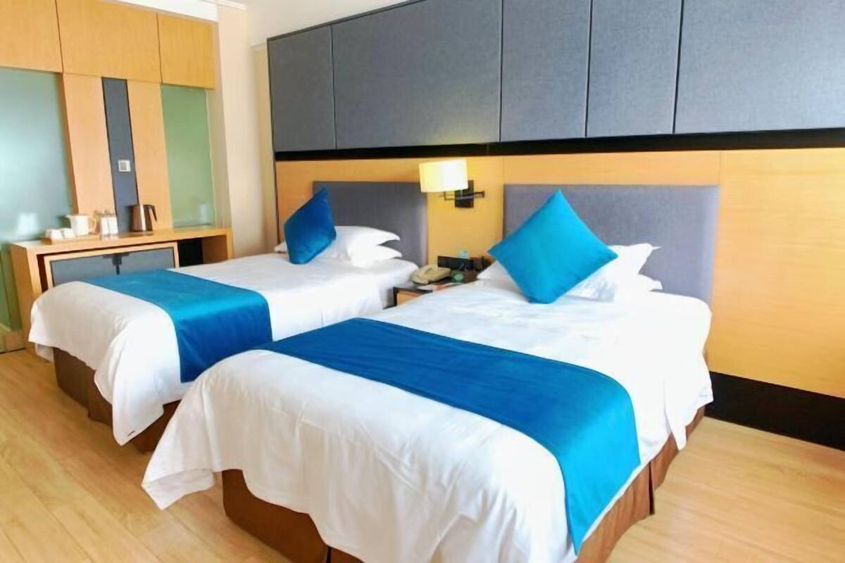Two beds with blue and white bedding, a bedside table with a lamp, and a wooden wardrobe.