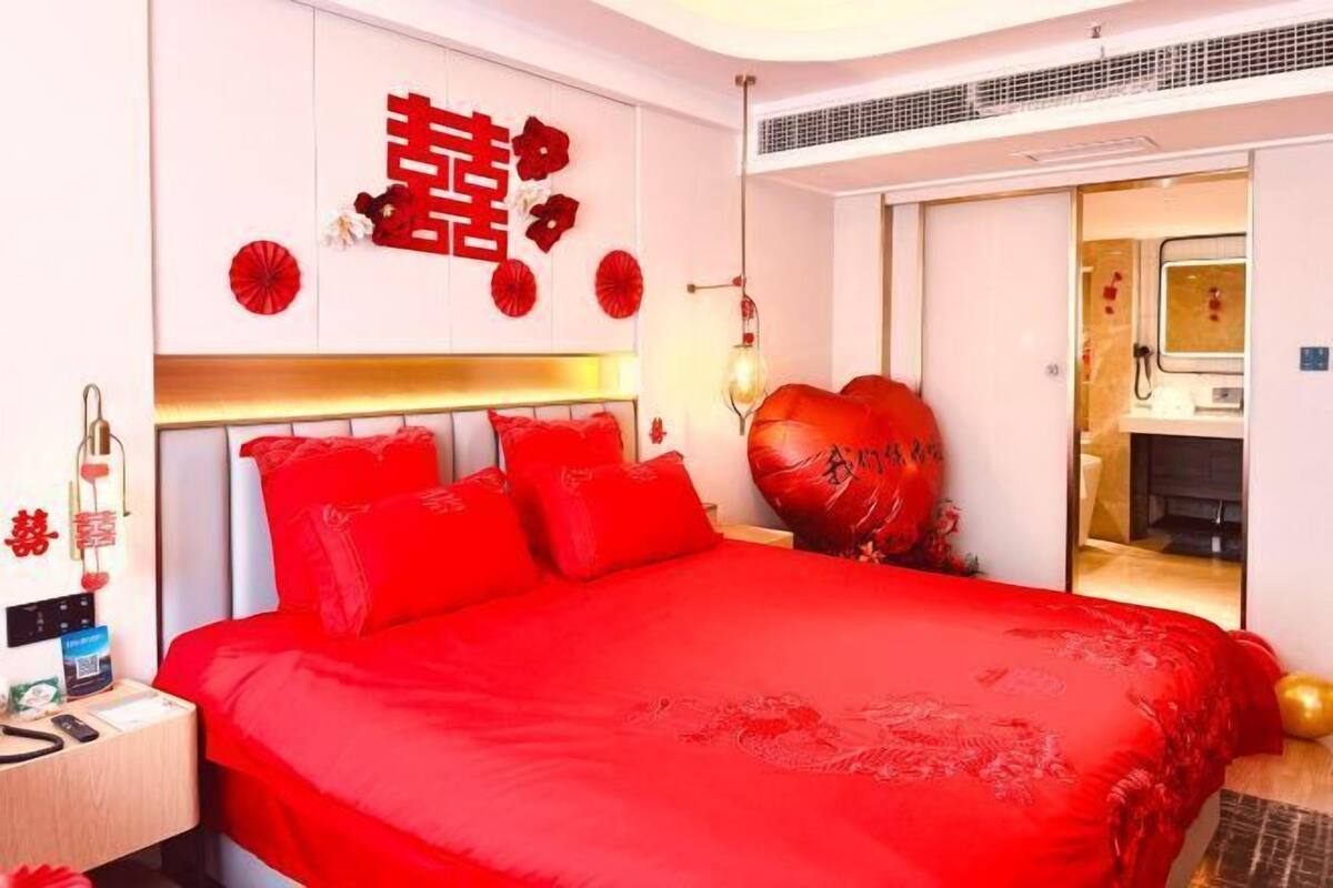 A hotel room with a large bed, a bedside table, a mirror, and a door leading to a bathroom.
