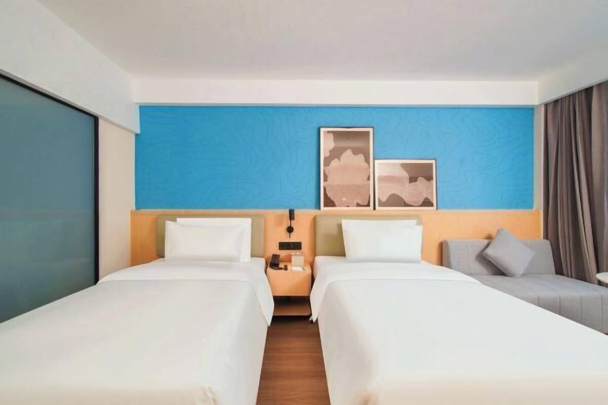 A hotel room with two beds, a nightstand, a desk, and a sofa.