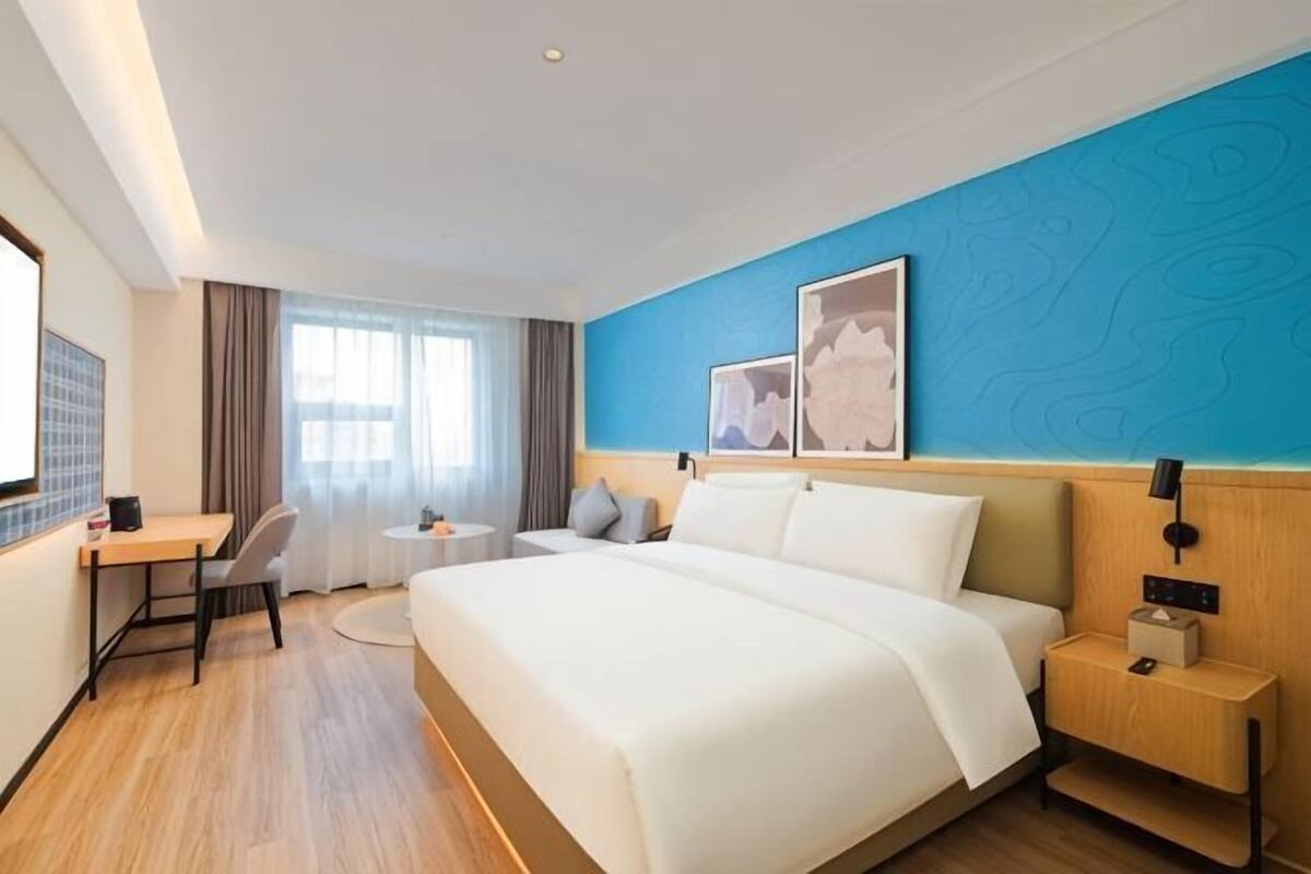 A hotel room with a large bed, a desk, a chair, a small table, and a window with curtains.