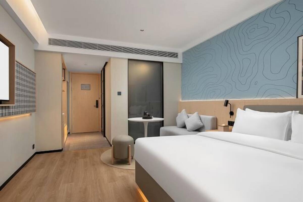 A modern hotel room with a large bed, a small table, a sofa, and a wall with a topographic design.