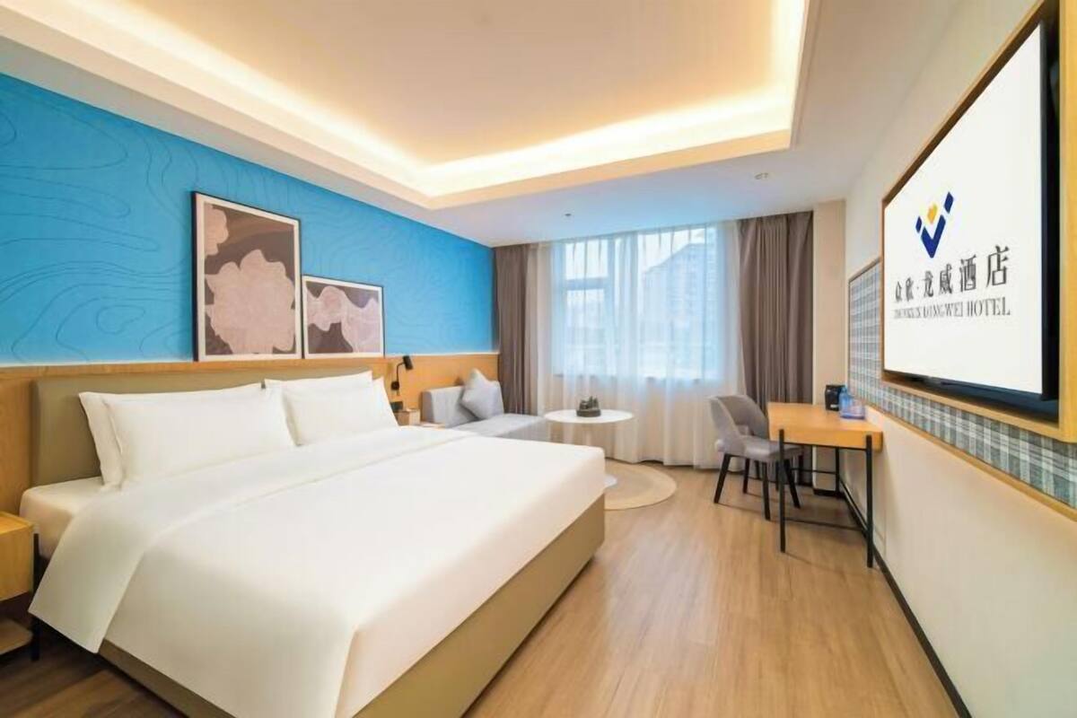 A hotel room with a large bed, a desk, a chair, and a TV.