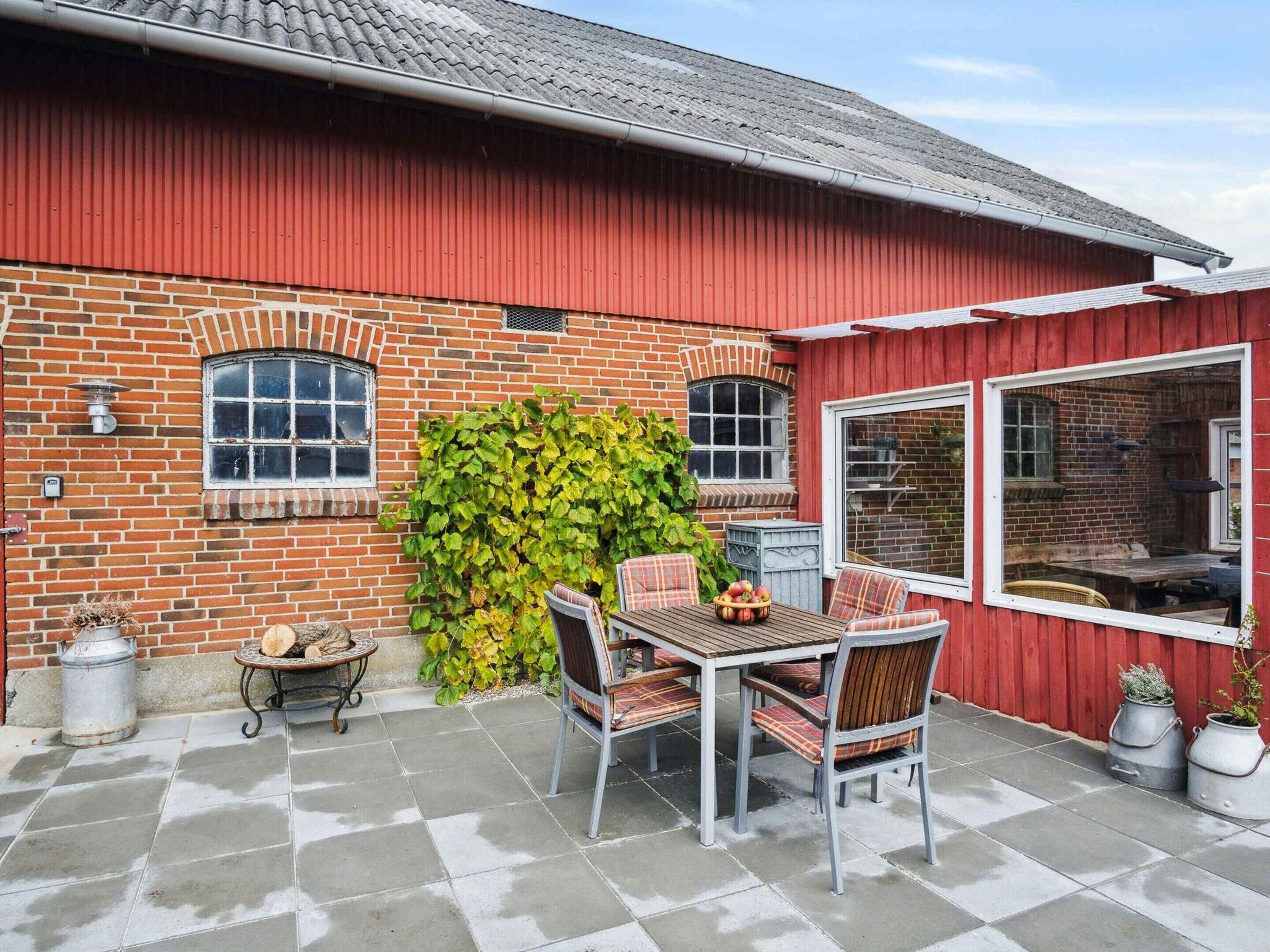 A brick house with a red exterior, a tiled patio, a table with chairs, and a large window.