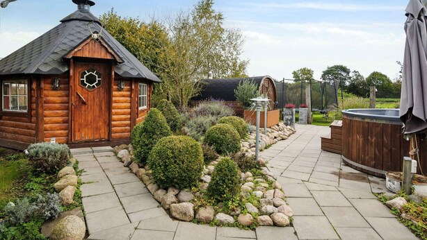 A wooden cabin with a hexagonal window, a stone pathway, and a hot tub. - 5 Star Holiday Home in Haderslev (Haderslev)