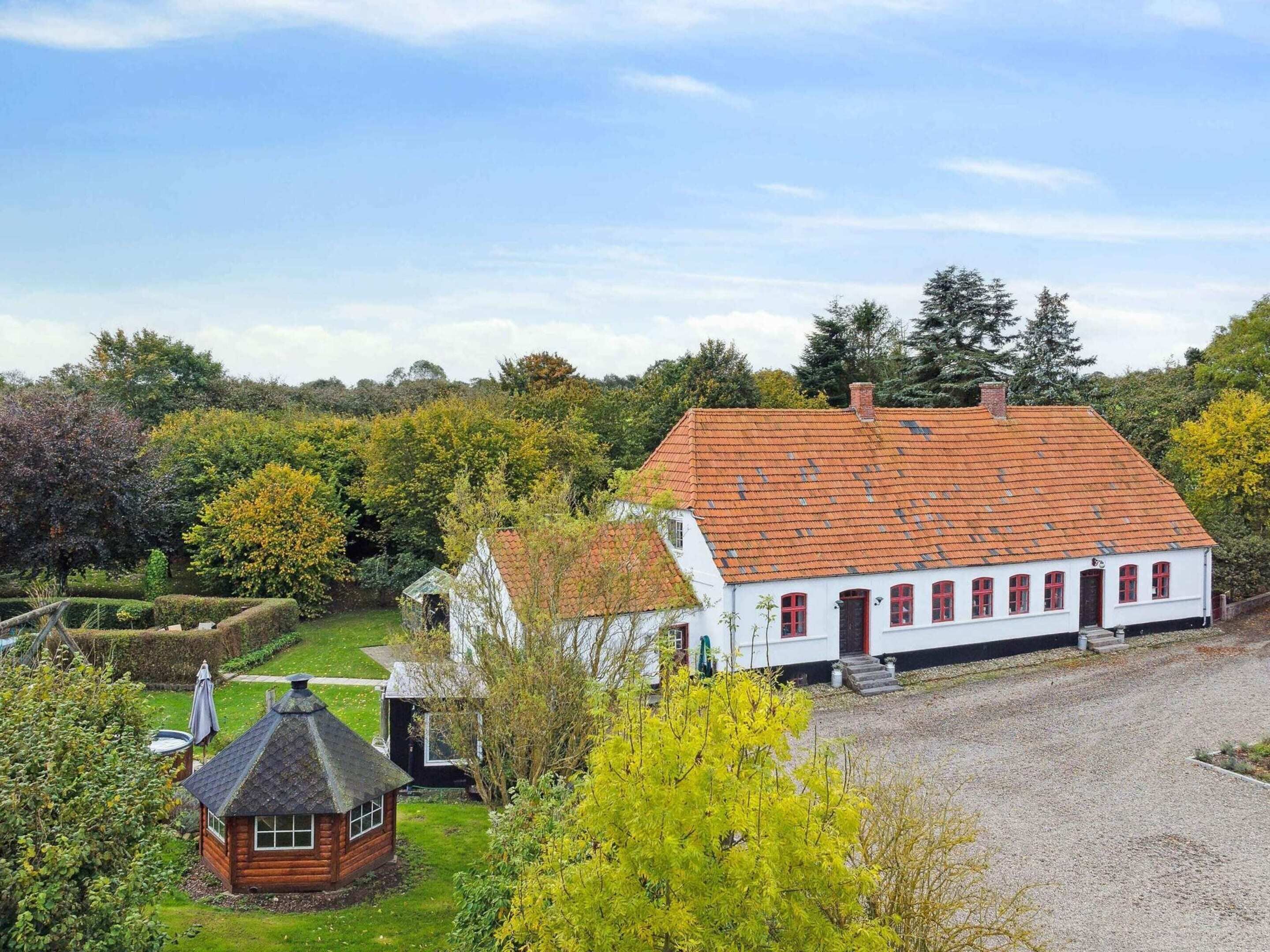 A traditional white building with a red-tiled roof, surrounded by lush greenery and trees.