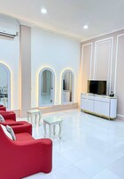 A spacious room with a white tiled floor, red sofas, a glass coffee table, and a white entertainment unit with a flat-screen TV.