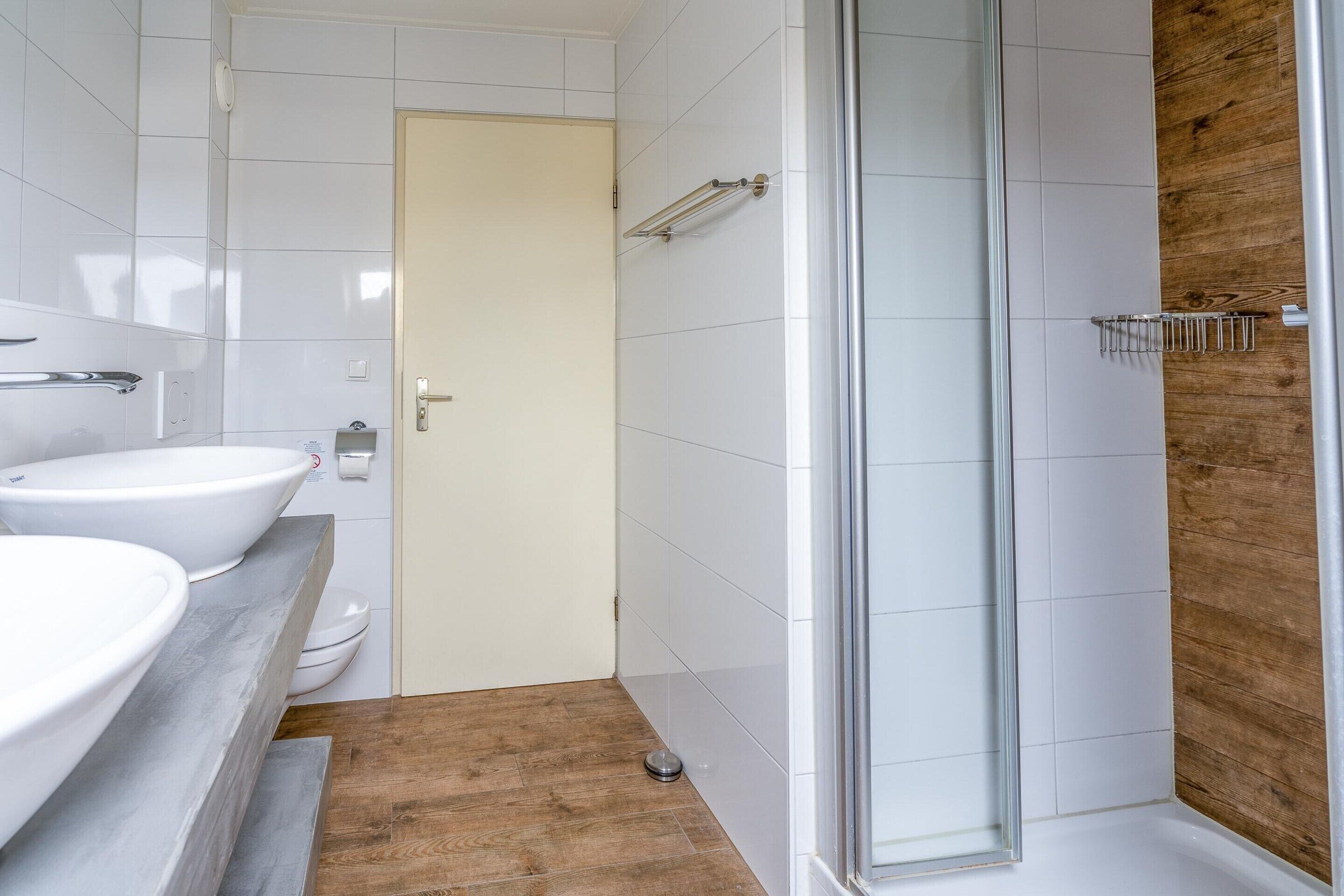 A bathroom with a shower, two sinks, and a toilet.
