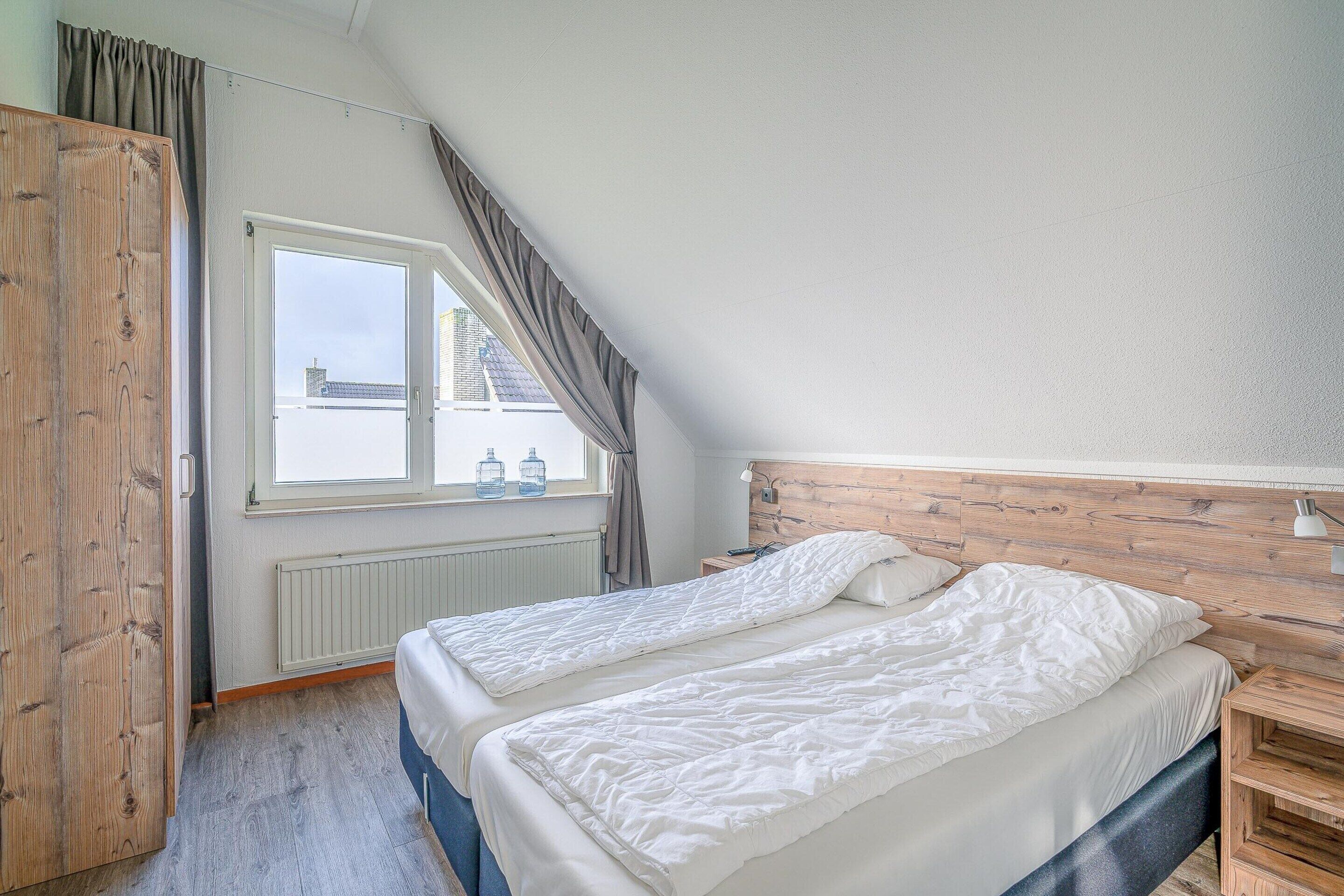 A bedroom with two beds, a wooden headboard, a window with curtains, and a radiator.