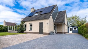A house with a sloped roof, solar panels, a small attached garage, and a paved driveway. - Charming Villa With Wood Stove Near the sea and Forest (De Koog)
