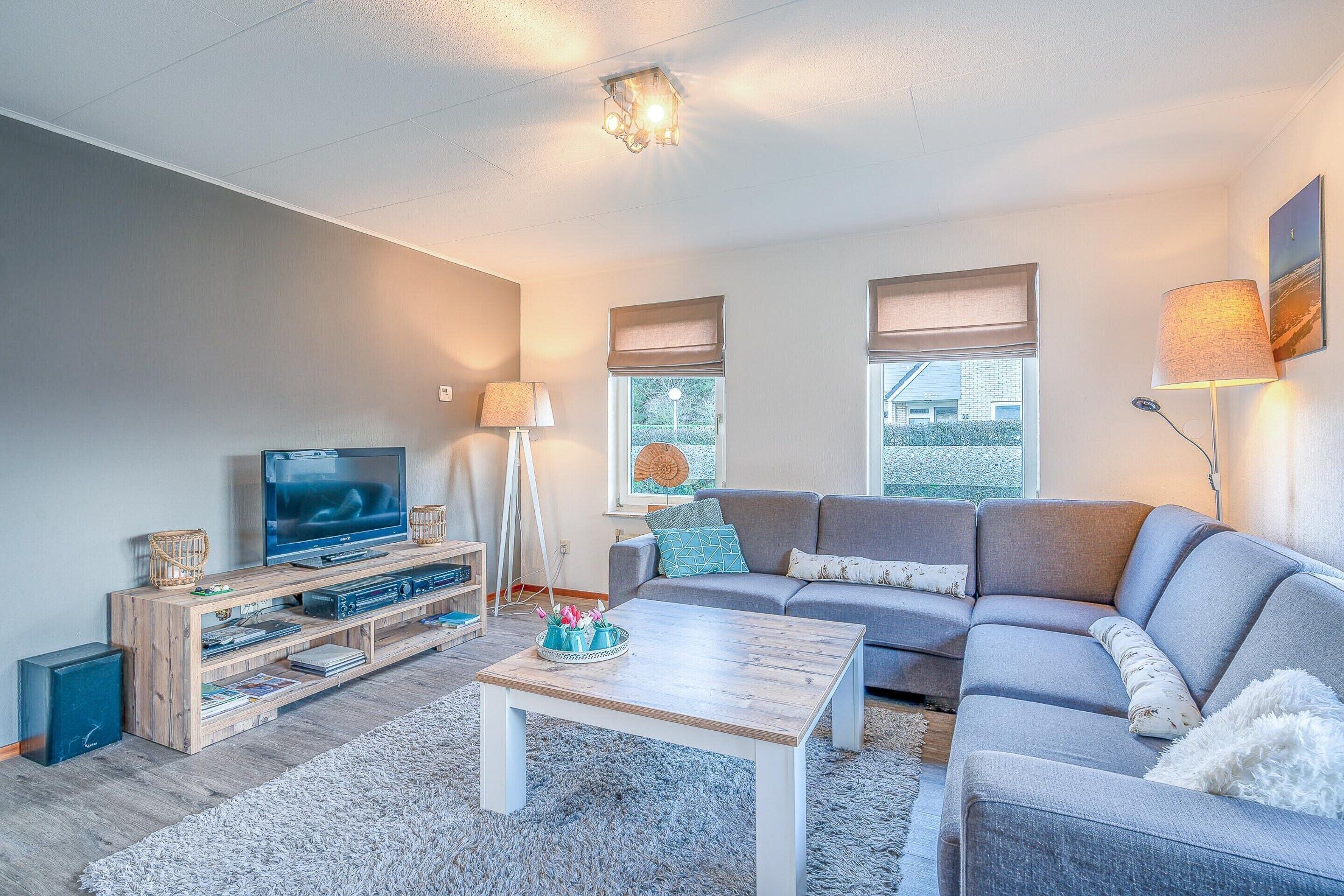 A modern living room with a grey sofa, a wooden coffee table, and a television on a wooden stand.