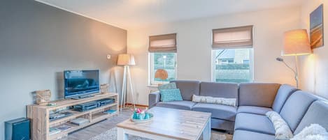 Un salon moderne avec un canapé gris, une table basse en bois et un téléviseur posé sur un meuble en bois.