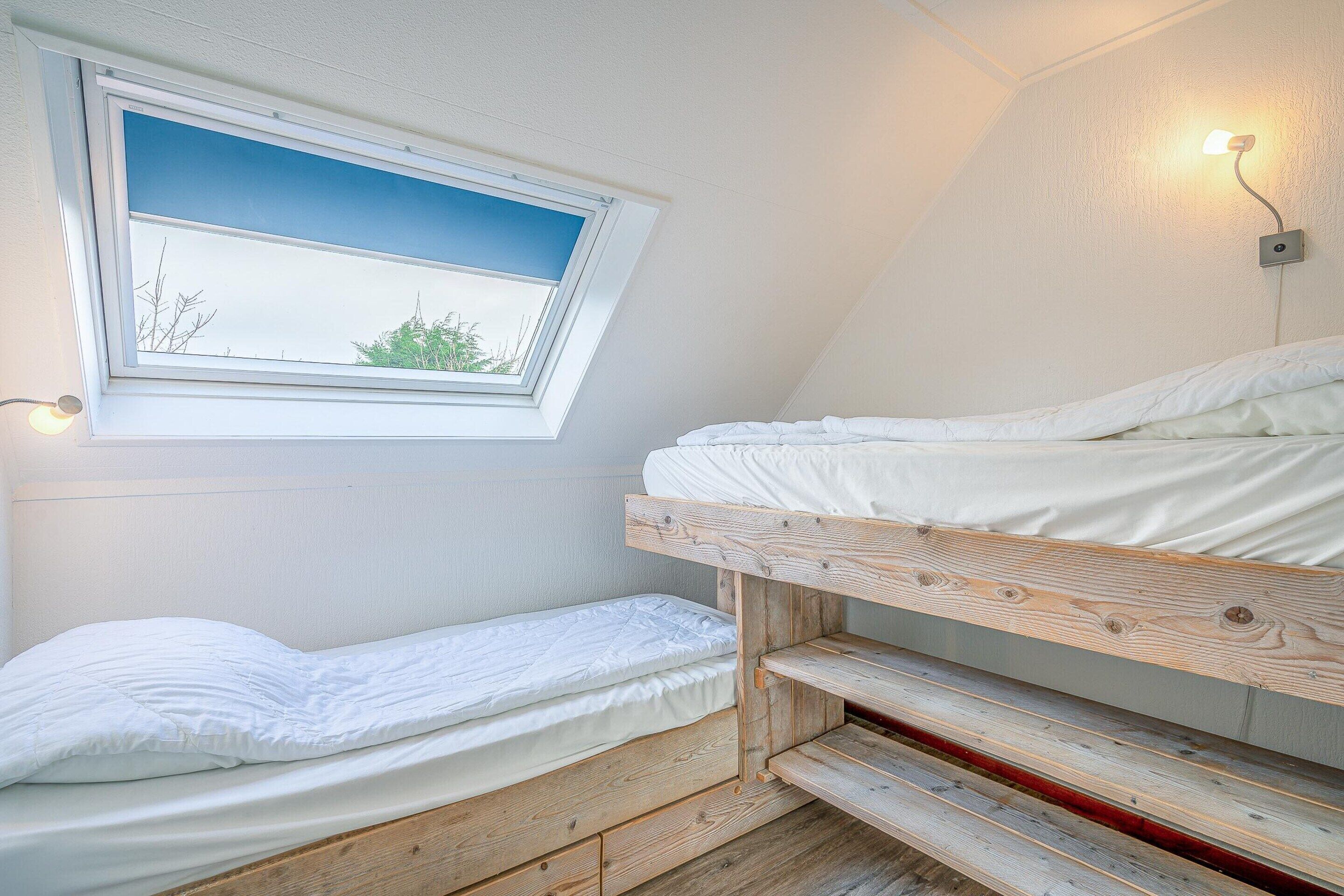 Une petite pièce unique, avec un plafond en pente, une fenêtre donnant sur un beau paysage et un lit doté d’une tête de lit en bois.