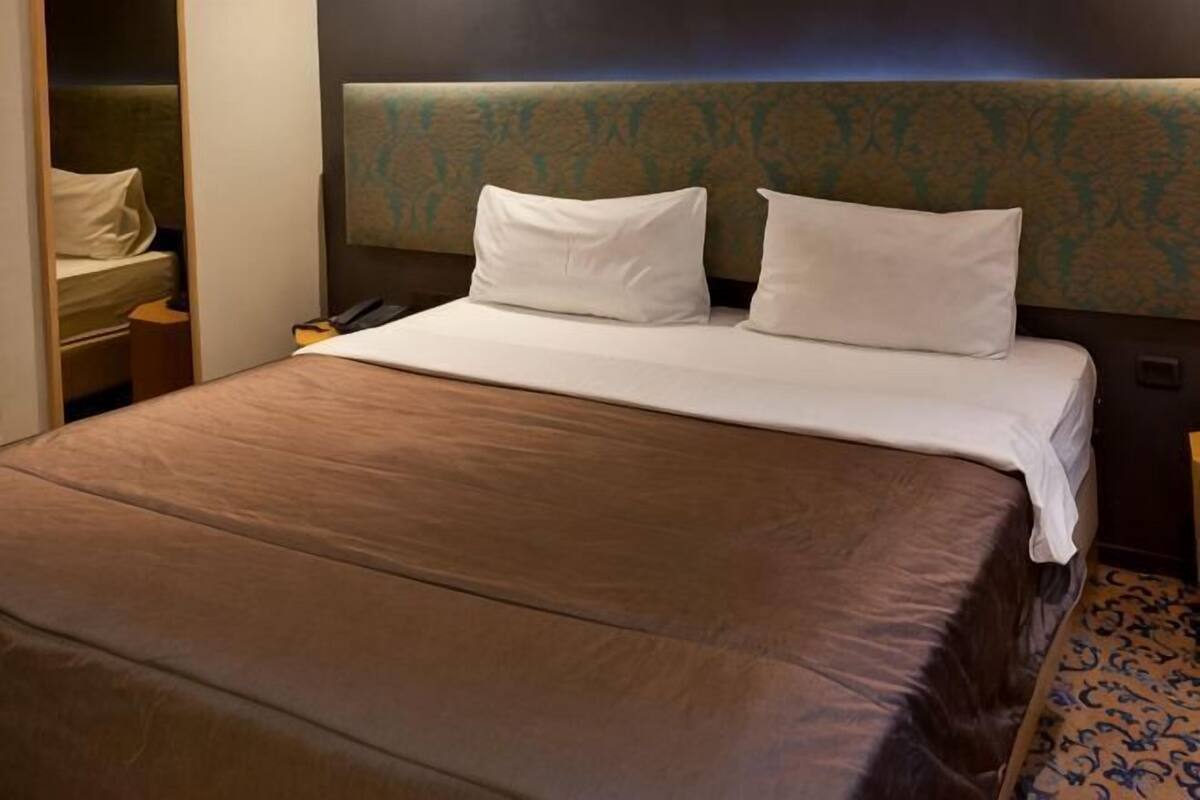 Habitación de hotel con una cama grande, cabecera con diseño estampado, mesita de noche con lámpara y otra mesita con teléfono.