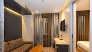 A modern hotel room with a sofa, a wooden bench, a desk with a chair, a bed, and a TV mounted on the wall. - Pera Tulip Hotel (Istanbul)