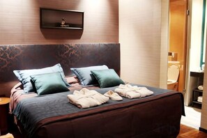Habitació d'hotel amb un llit, dos coixins, una taula de nit i una prestatgeria penjada a la paret.