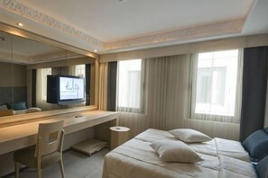 Ein Hotelzimmer mit Bett, Schreibtisch, Stuhl, Fernseher und großen Fenstern.