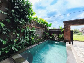 A swimming pool with a stone border, surrounded by lush greenery and a brick wall. - Amaluku Villa (Ubud)