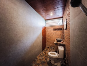 A small bathroom with a tiled floor, a white toilet, a sink with a basin, and a wooden ceiling. - Amaluku Villa (Ubud)