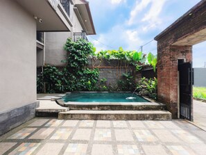 A swimming pool with a tiled deck, surrounded by lush greenery and a brick wall. - Amaluku Villa (Ubud)
