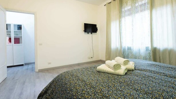 Une chambre à coucher avec un lit, un téléviseur fixé au mur et une fenêtre avec des rideaux.