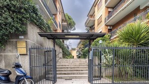 Une entrée fermée par un portail menant à un immeuble résidentiel, avec un scooter garé à l’extérieur.