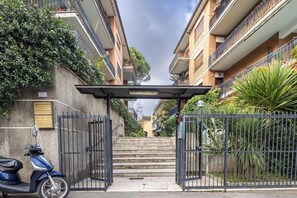 Une entrée fermée par un portail menant à un immeuble résidentiel, avec un scooter garé à l’extérieur.