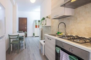 Une cuisine de taille réduite, équipée d’une cuisinière à gaz, d’un évier et d’un coin repas avec des chaises.