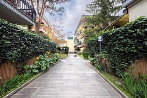 A pathway flanked by lush greenery and residential buildings.