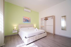 Une chambre à coucher comprenant un lit, des tables de chevet, un appareil de climatisation, une armoire et un tableau accroché au mur.