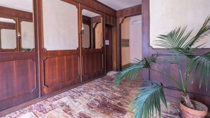 Un couloir avec des portes en bois, une plante en pot et un sol en marbre.