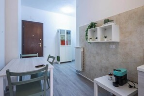 A room with a wooden door, a white cabinet, a table with chairs, a shelf with plants, and a coffee machine. - BuddyRent - Garden House - Vaticano - 3 ospiti (Roma)