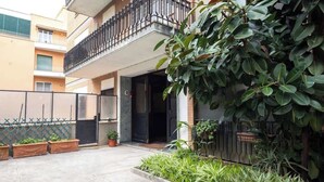 Un immeuble résidentiel doté d’un balcon, de plantes en pot et d’une entrée fermée par un portail.