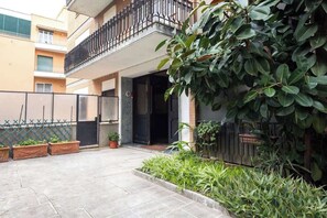 Un immeuble résidentiel doté d’un balcon, de plantes en pot et d’une entrée fermée par un portail.