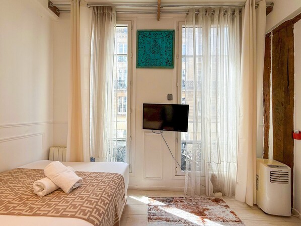 A hotel room with a bed, a TV mounted on the wall, a radiator, and a window with curtains.