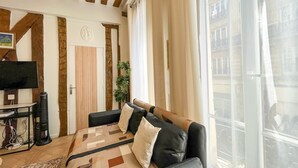 Ein Wohnzimmer mit einer Couch, einem Fernseher, einer Pflanze und einem Fenster mit Blick auf Gebäude.