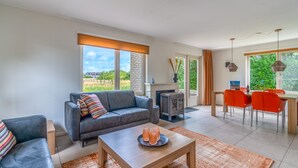 A modern living room with a grey sofa, a coffee table, and a dining area with orange chairs. - Charming Villa With Sauna on the Water (De Koog)
