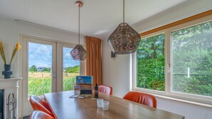A dining area with a wooden table, red chairs, and hanging pendant lights. - Charming Villa With Sauna on the Water (De Koog)