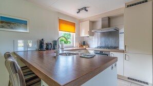 A modern kitchen with a wooden island, stainless steel appliances, and a window with a view of greenery. - Charming Villa With Sauna on the Water (De Koog)