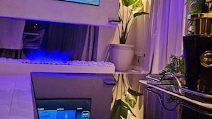 Moderni olohuone, jossa on taulutelevisio, pieni pöytä kannettavalle tietokoneelle ja ruukussa oleva kasvi.
