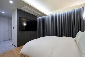 A modern hotel room with a large bed, a flat-screen TV mounted on the wall, and a dark curtain backdrop. - Hotel Tara (Seoul)