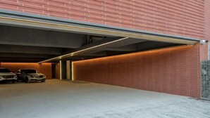A covered parking garage with three cars, a brick wall, and a concrete floor. - Hotel Tara (Seoul)