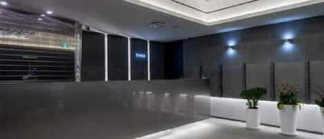 A modern lobby with a reflective floor, a reception desk, and potted plants.